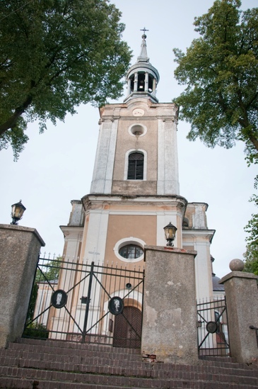 Wieża kościoła świętego Krzyża i Mikołaja w Biezdrowie. Widoczna fafada wieży z chełmem. Na pierwszym palnie widoczne schody i metalowa furta z murkiem. 